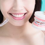 Woman holds up Invisalign clear aligners and a teeth model with braces to compare their benefits
