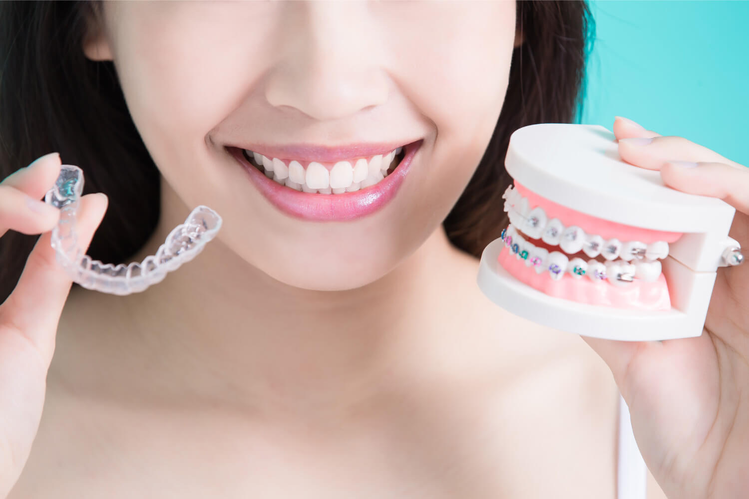 Woman holds up Invisalign clear aligners and a teeth model with braces to compare their benefits
