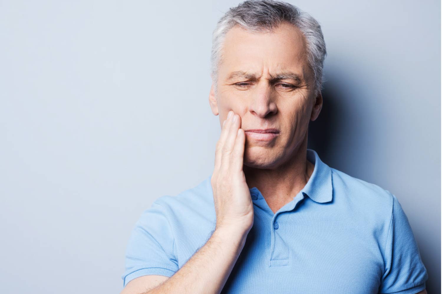Mature man with his hand to his cheek indicating tooth pain.
