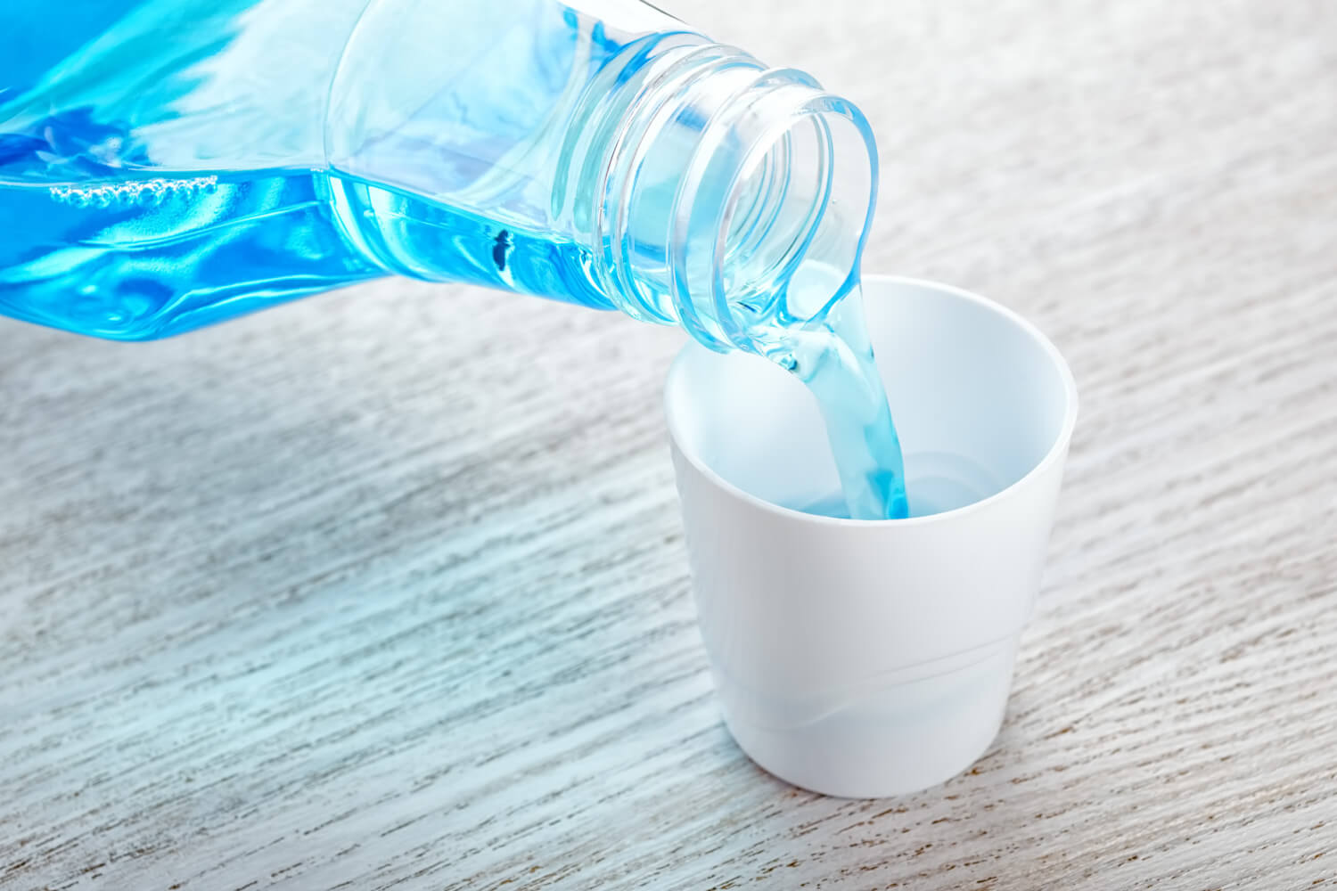 Blue mouthwash being poured into a white cup to rinse away plaque and food particles