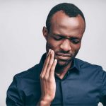 Black man holding the side of his cheek because of tooth pain.