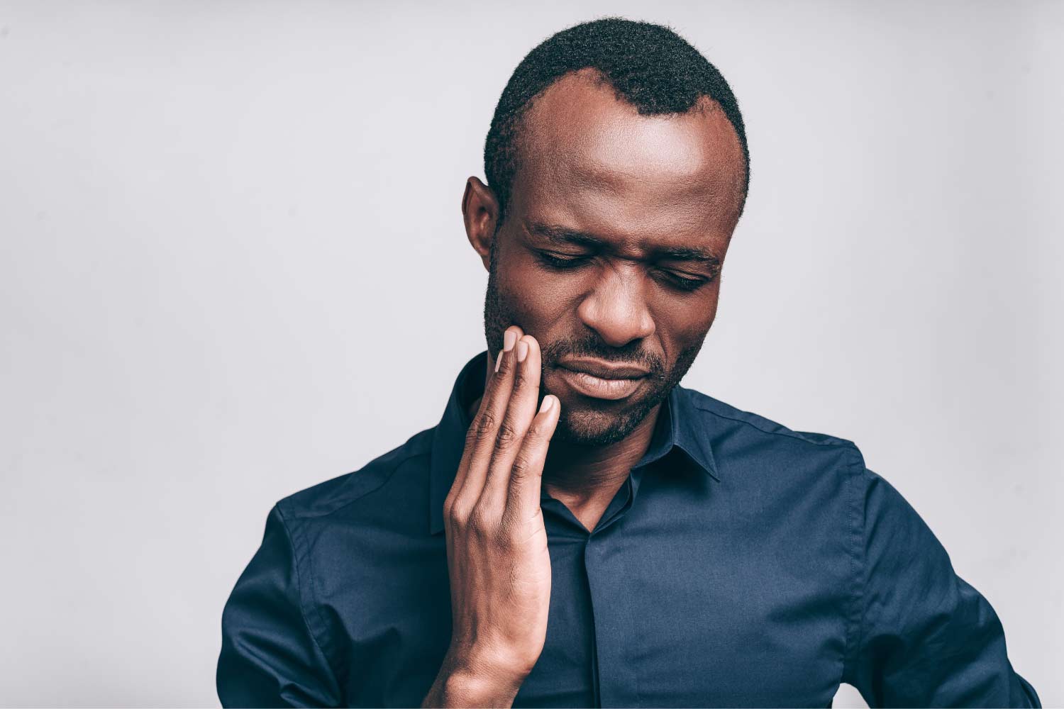 Black man holding the side of his cheek because of tooth pain.